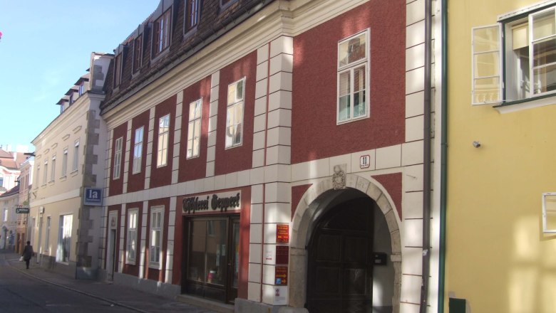 Historisches Gebäude mit roter Fassade und Torbogen in einer Altstadtstraße., © Mondseer Stiftshof