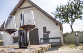 Zwei Weingläser und eine Flasche auf Holztisch vor kleinem Gebäude., © Donau Niederösterreich, Robert Herbst