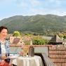 Frau genießt Wein auf Terrasse mit Blick auf grüne Hügel und Dorf., © DI Doris Hamberger