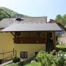 Gelbes Haus mit Balkon, umgeben von grüner Landschaft und Steinmauer., © Bergkirchner